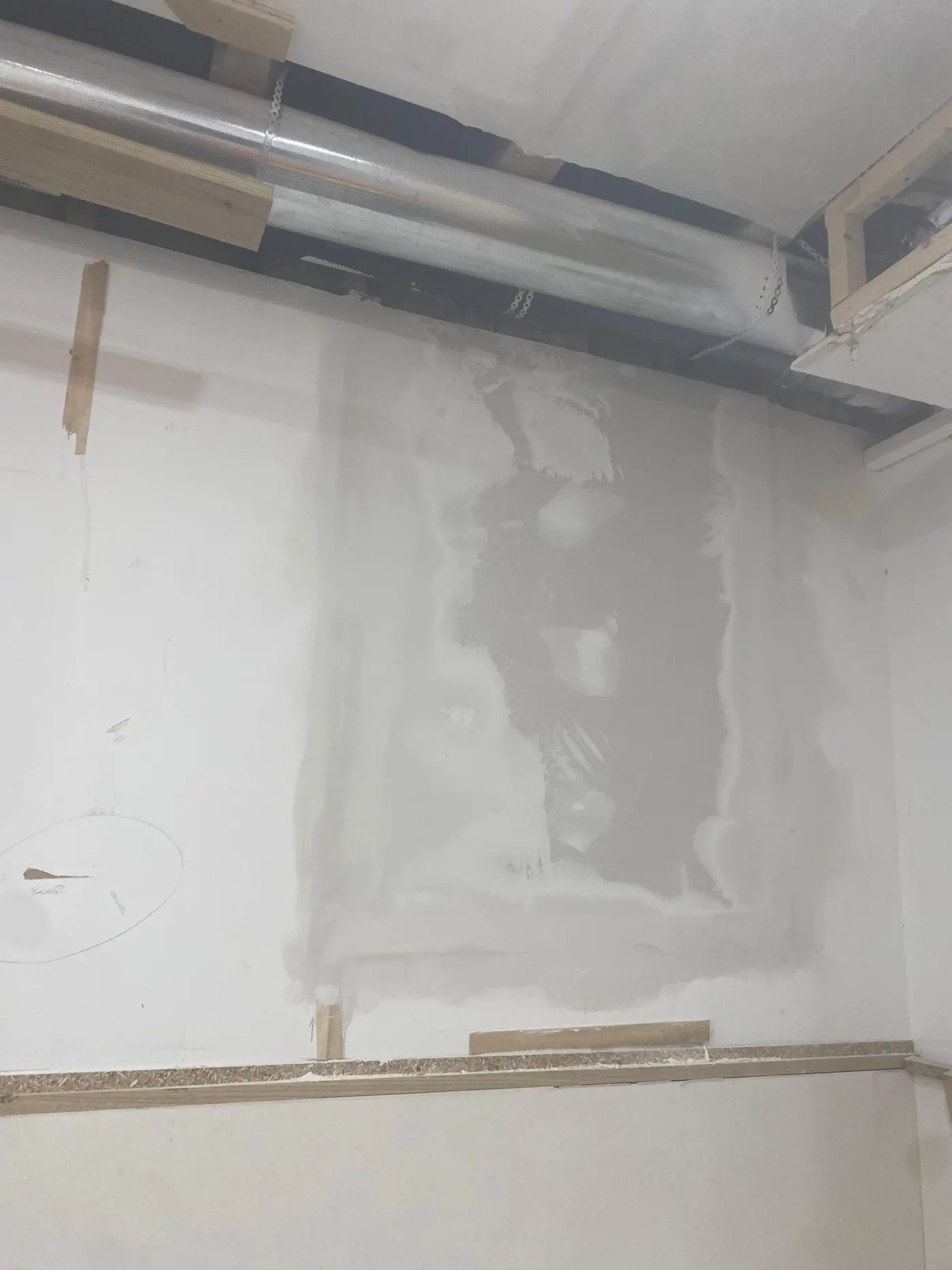 Repaired basement wall with fresh joint compound smoothed over the patched drywall, sanded and ready for primer