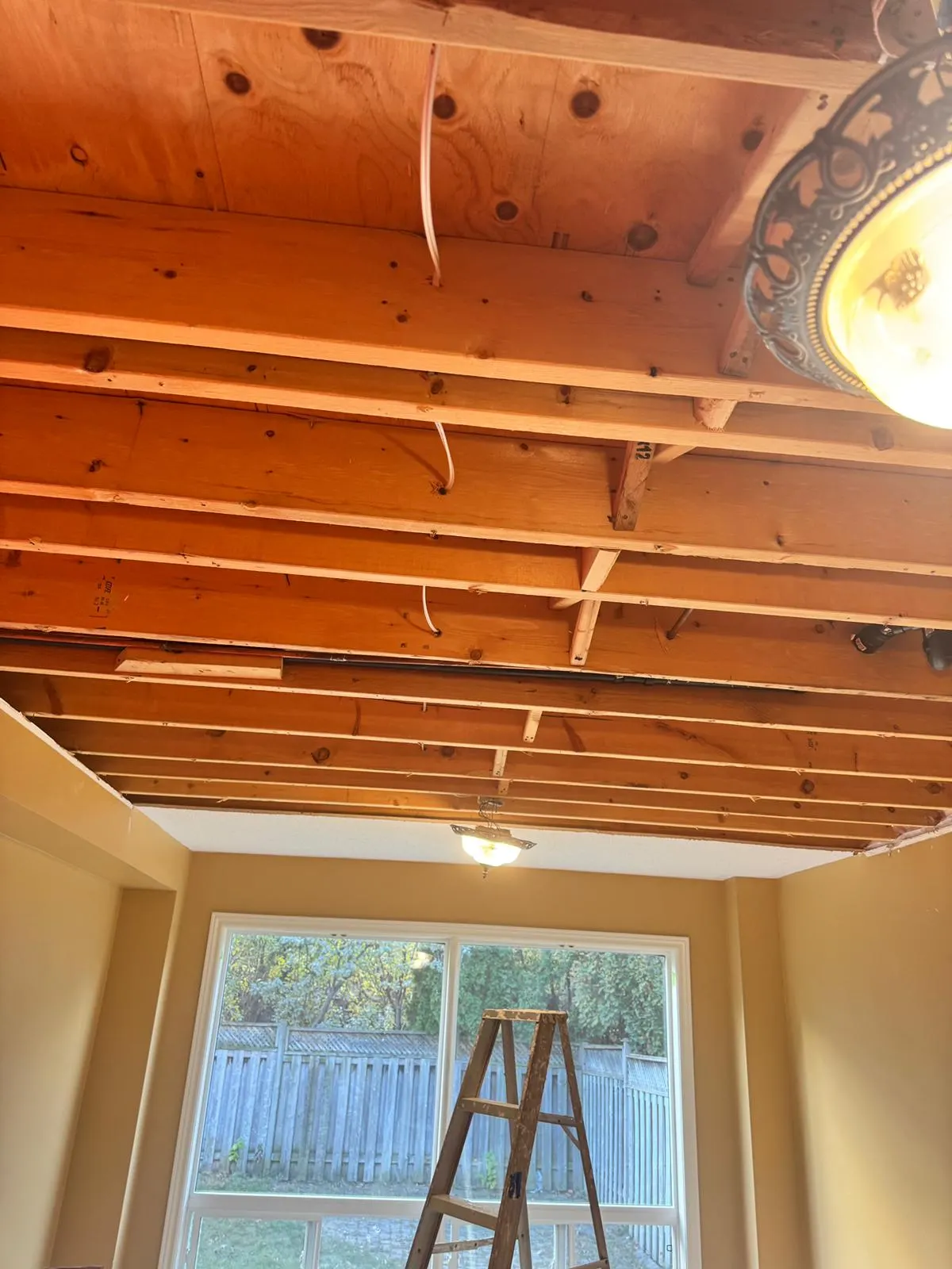 Ceiling drywall removed to expose the floor joists and subfloor above after water came through from an upper floor, stepladder standing in the room